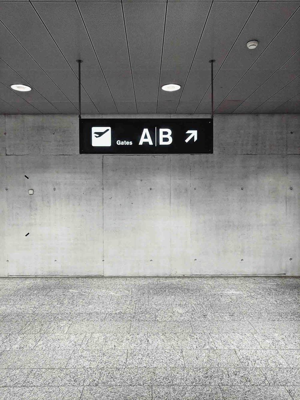 En flygplatsskylt som visar vägen till gates A och B, med en pil som pekar åt höger, monterad i ett modernt och minimalistiskt utrymme.
