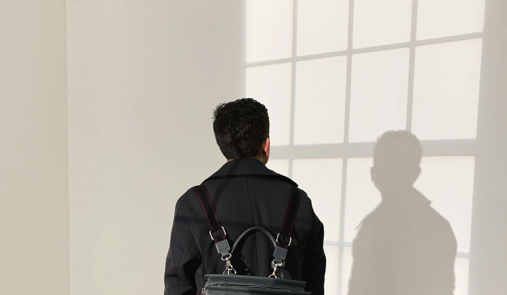 Person med ryggsäck står framför ett fönster och betraktar sin skugga som faller på väggen.