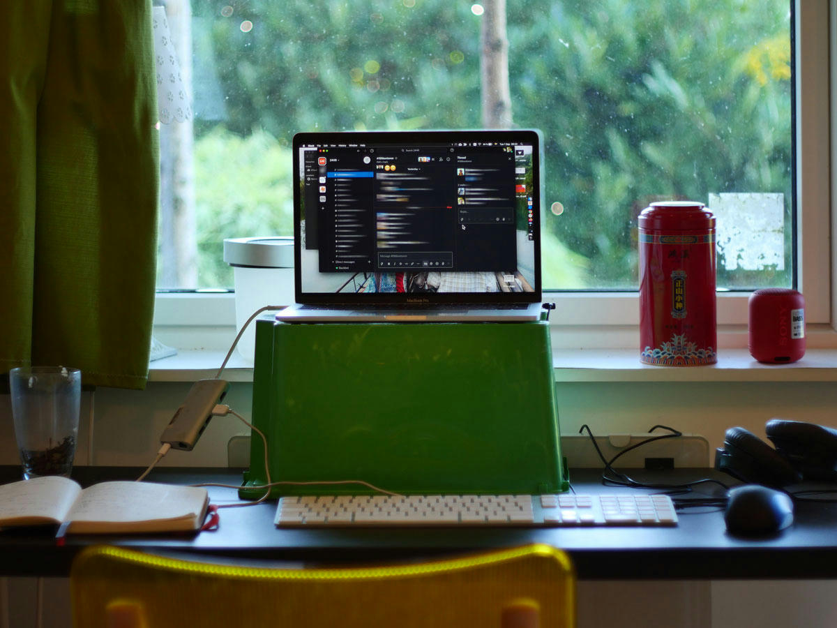 Arbetsstation med en bärbar dator på en upphöjd plattform, ett tangentbord, en mus, en anteckningsbok och ett glad med lyxigt te. Fönster i bakgrunden med utsikt över grönska och olika föremål på fönsterbrädan. Arbetsstation med en bärbar dator på en upphöjd plattform, ett tangentbord, en mus, en anteckningsbok och ett glad med lyxigt te. Fönster i bakgrunden med utsikt över grönska och olika föremål på fönsterbrädan.