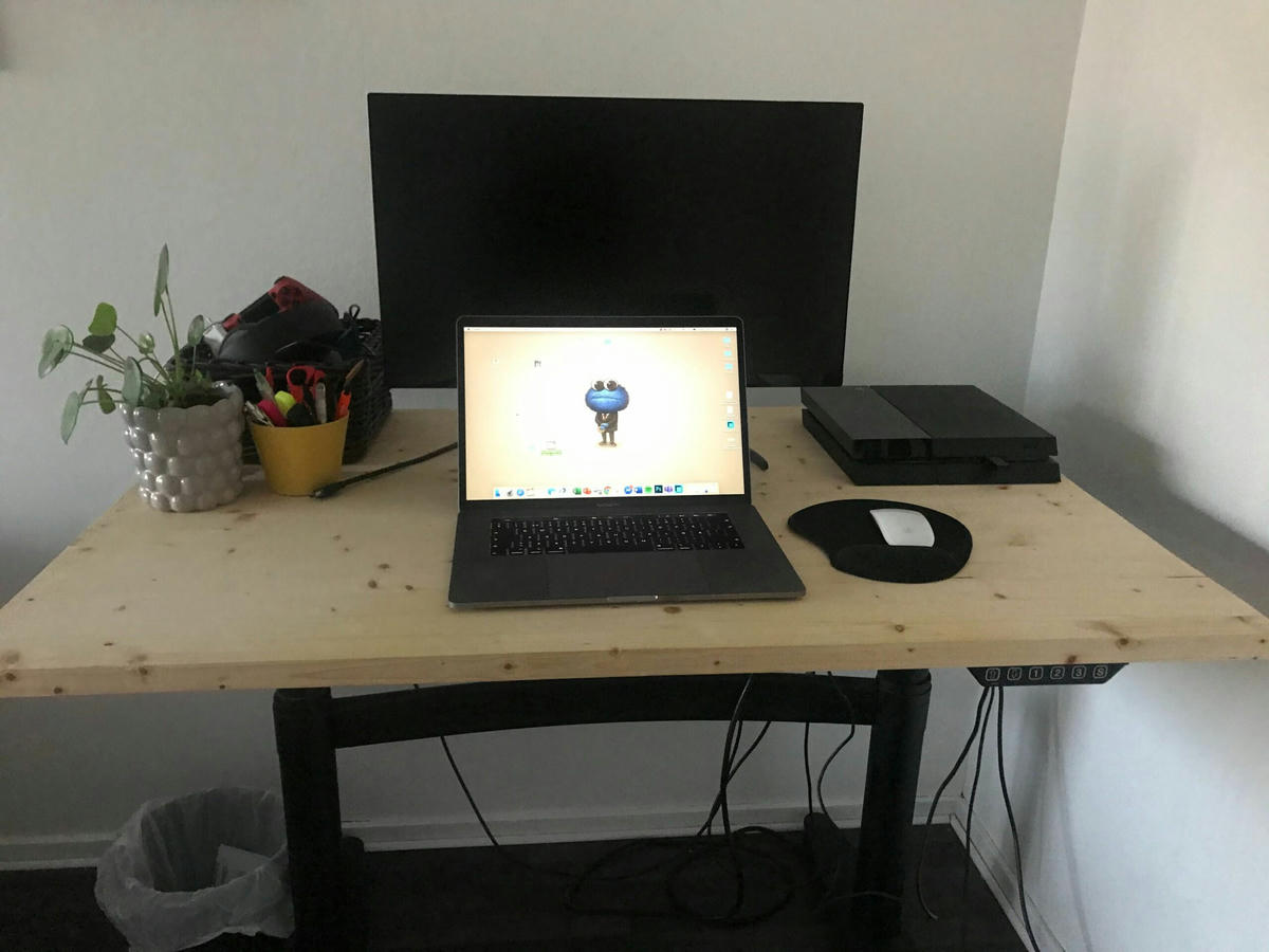 Arbetsstation med en bärbar dator framför en extern bildskärm, en spelkonsol, en mus med musmatta, en krukväxt och en behållare med kontorsmaterial på ett höj- och sänkbart skrivbord. Arbetsstation med en bärbar dator framför en extern bildskärm, en spelkonsol, en mus med musmatta, en krukväxt och en behållare med kontorsmaterial på ett höj- och sänkbart skrivbord.