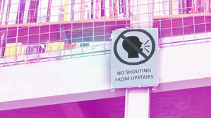 Skylt med texten ‘No shouting from upstairs’ och en symbol som förbjuder ropande, uppsatt på ett räcke med böcker i bakgrunden.